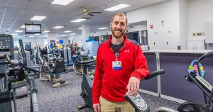 Mission Partner poses in front of rows of ellipticals, treadmills and weightlifting machines