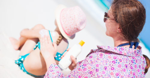 mom applying sunscreen to daughter at beach