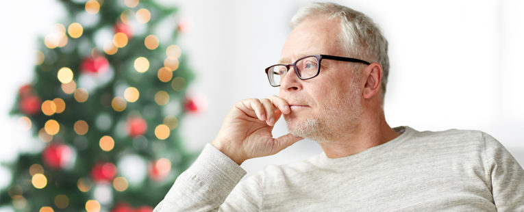 Senior gentleman contemplating next to a Christmas tree.