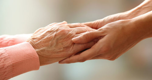 elderly woman's hands being held by a hospice volunteer.