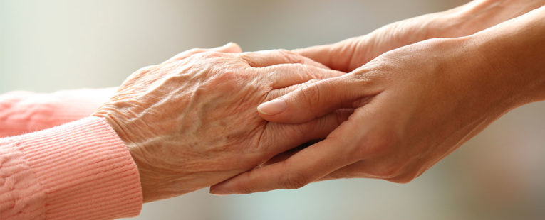 elderly woman's hands being held by a hospice volunteer.