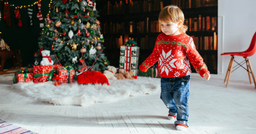 Toddler in sweater by a Christmas tree.