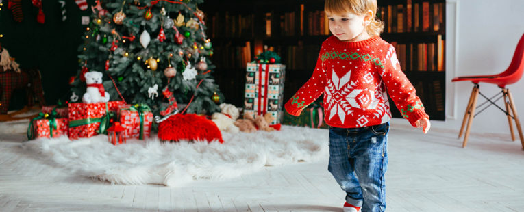 Toddler in sweater by a Christmas tree.