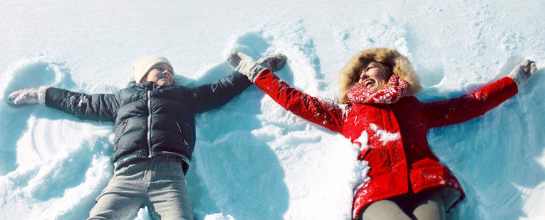 Mother and daughter making snow angels in winter.