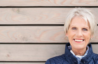 Older woman standing outside wearing a winter coat smiling.