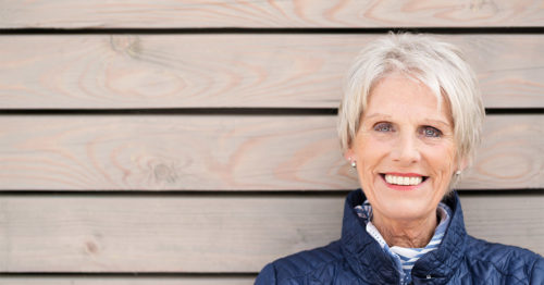 Older woman standing outside wearing a winter coat smiling.
