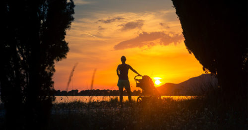 woman and child in stroller on a beach at sunset