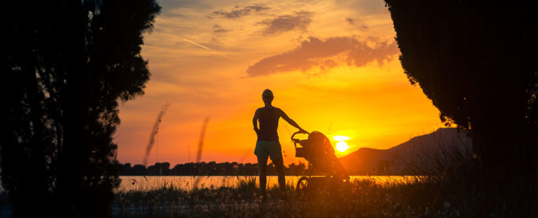 woman and child in stroller on a beach at sunset