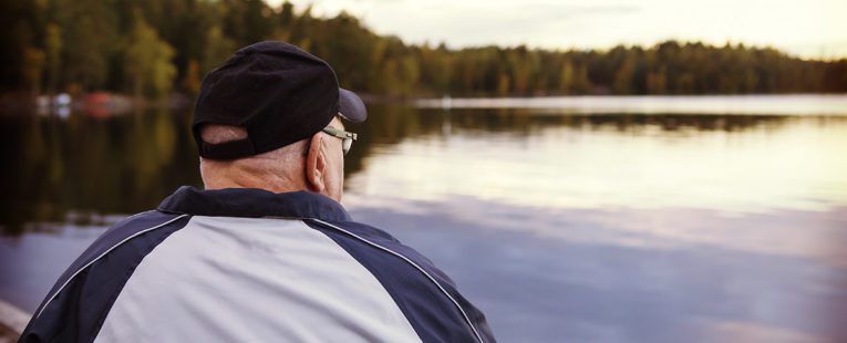 senior man contemplating while staring at a lake outside