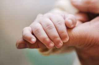 Infant hand wrapped around a finger of a congential heart specialist