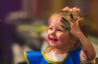 Cheerful Adalie Guth playing with finger paint at home.