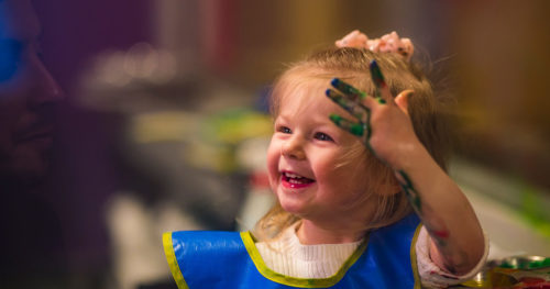 Cheerful Adalie Guth playing with finger paint at home.