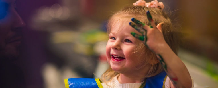 Cheerful Adalie Guth playing with finger paint at home.