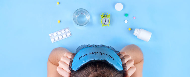 woman who cannot sleep looking at melatonin and other sleep aids on a tabletop.