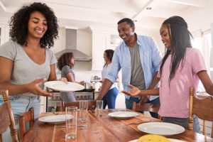 African-American family clearing dishes from the breakfast table after mindful eating.