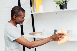 African-American man dusting bookshelves in apartment