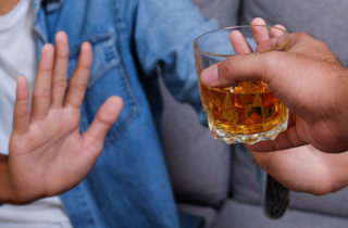 person saying no to friend offering glass of whiskey