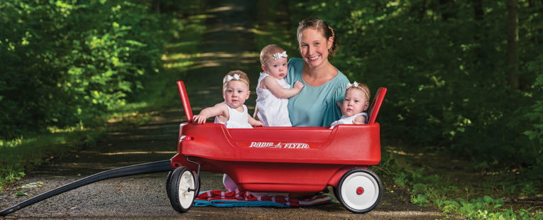 Colwell triplets and their mother in a wagon outdoors.