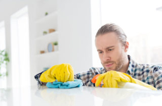 Young man learning how to clean a kitchen countertop with gloves and cleaning solution.