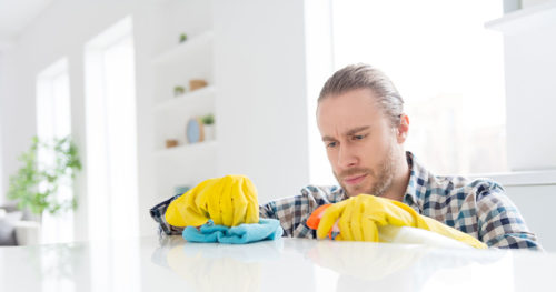 Young man learning how to clean a kitchen countertop with gloves and cleaning solution.