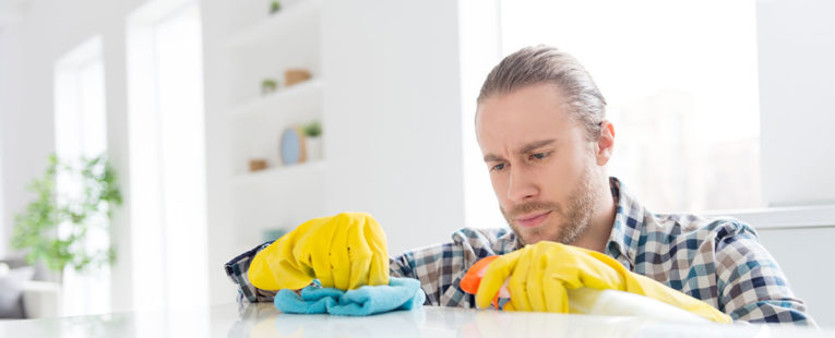 Young man learning how to clean a kitchen countertop with gloves and cleaning solution.