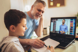 Father helps young son with distance learning on computer.