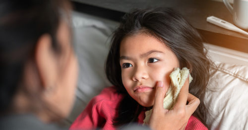 Mother wiping young daughter's cheek with cool washcloth to determine what the sick person needs.
