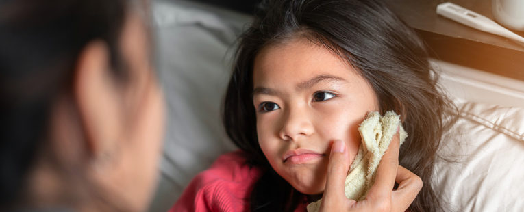 Mother wiping young daughter's cheek with cool washcloth to determine what the sick person needs.