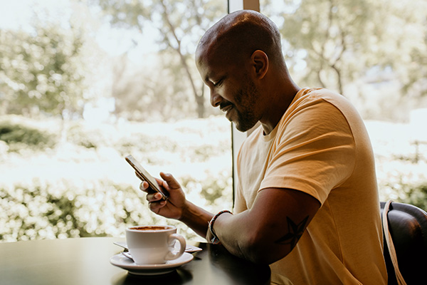 Young African-American man in coffee shop checking news feed on his phone.