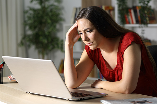 Young concerned woman reading news on laptop.