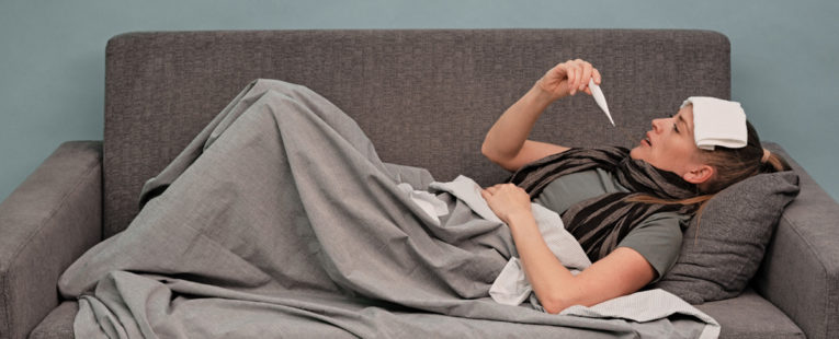 Woman with fever taking temperature on couch.