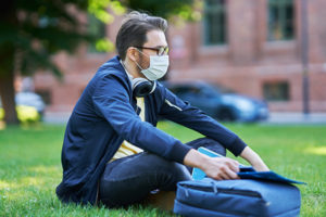 Young masked college male student outdoors.