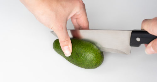 hand with knife using the proper method to safetly cut into an avocado