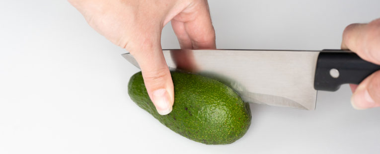 hand with knife using the proper method to safetly cut into an avocado