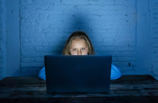 Young girl on a computer in a dark room doing online learning.
