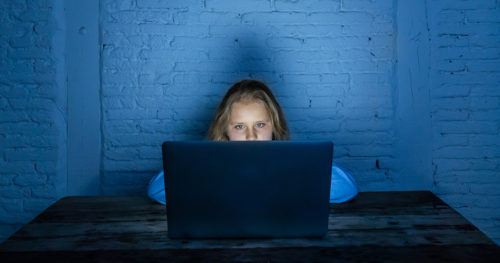 Young girl on a computer in a dark room doing online learning.