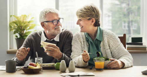 male and female seniors eating healthy food smiling at each other