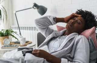 visibily sick woman in a bath robe surrounded by tissues suffers ailment reclined in a chair