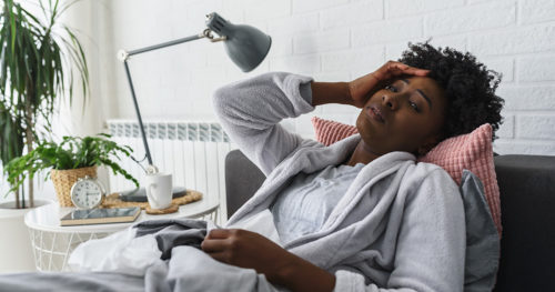 visibily sick woman in a bath robe surrounded by tissues suffers ailment reclined in a chair