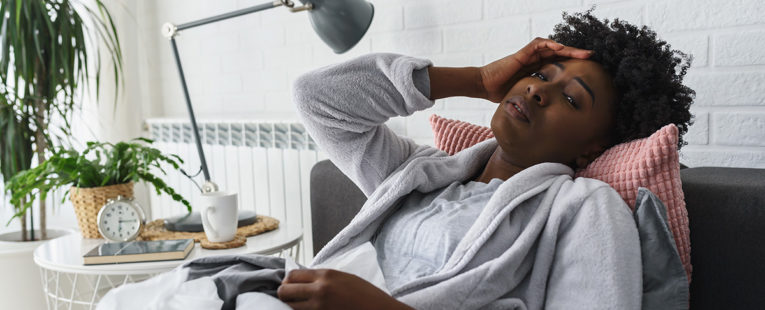 visibily sick woman in a bath robe surrounded by tissues suffers ailment reclined in a chair