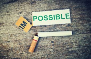 cigarette broken in half next to an impossible sign ripped to read possible