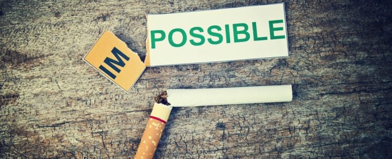 cigarette broken in half next to an impossible sign ripped to read possible