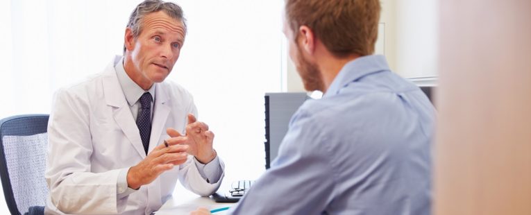 male physician sitting down and conversing with a male patient