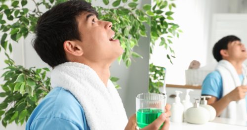 man with towel around neck gargles mouthwash in bathroom