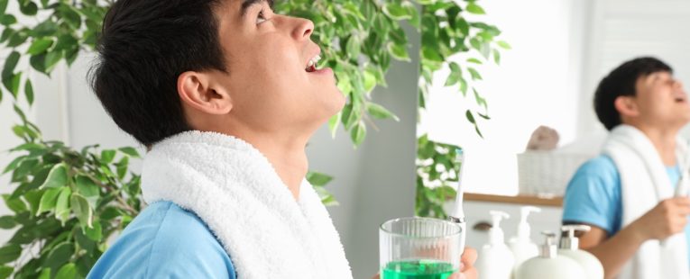 man with towel around neck gargles mouthwash in bathroom