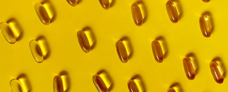 Vitamin D capsules on yellow background.