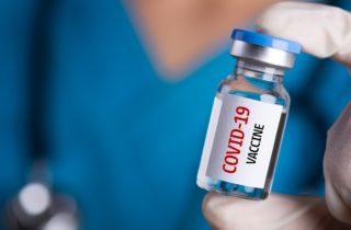 care team wonrker holding a vial with "COVID-19 vaccine" printed on it