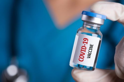 care team wonrker holding a vial with "COVID-19 vaccine" printed on it