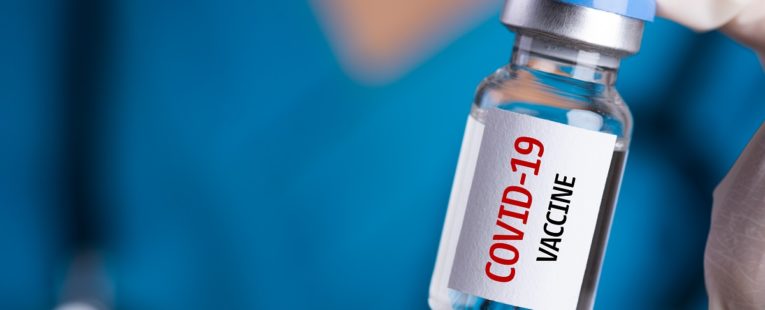 care team wonrker holding a vial with "COVID-19 vaccine" printed on it