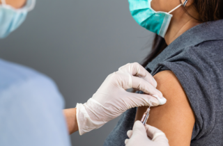 masked doctor gives a masked patient a vaccine with a needle